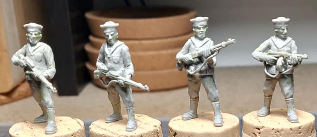 Five unpainted miniature soldier figures standing on cork bases on a tabletop in a workshop setting.